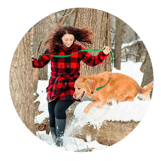 Dog mom with golden retriever jumping over snowy log