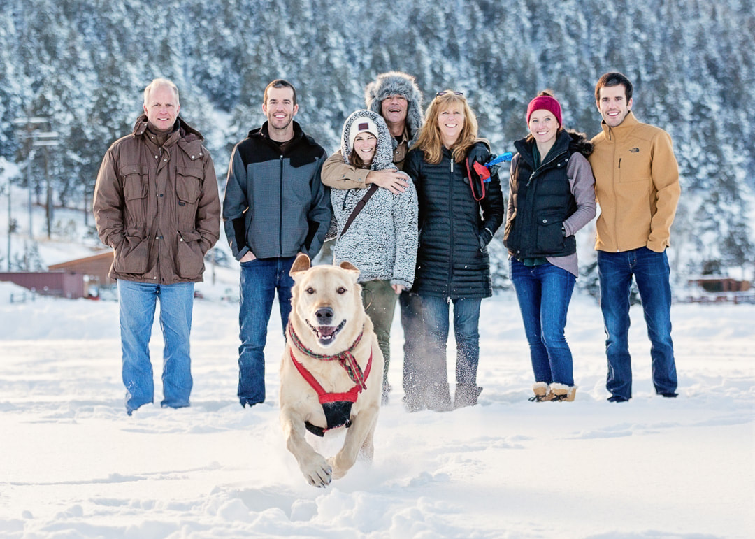 white lab dog running in the snow with his family smiling behind him