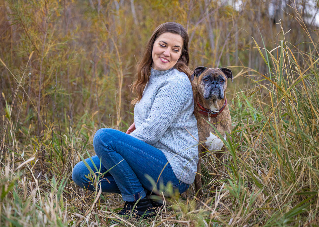 Brindle boxer dog standing next to her dog mom who is sitting in the tall grasses